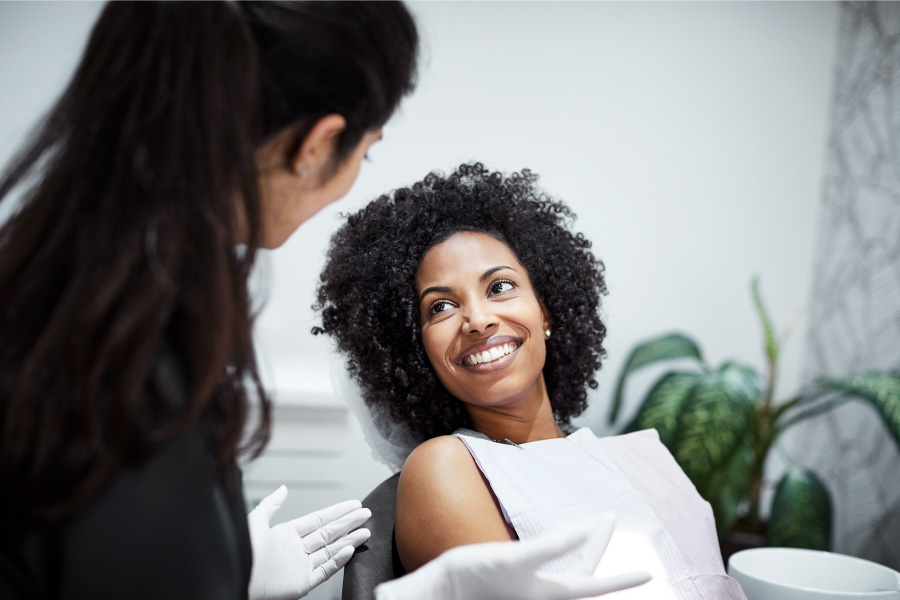 Curly-haired woman smiles before receiving her dental cleaning at the dentist