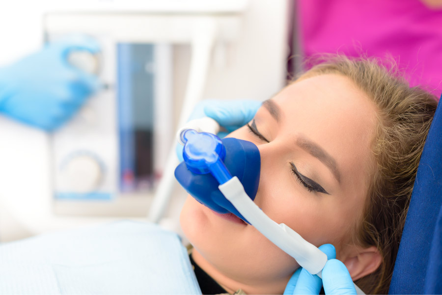 Brunette woman relaxes as she inhales nitrous oxide through a blue nose mask