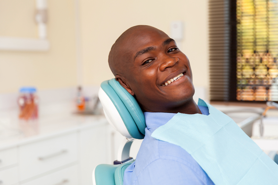 Bald Black man smiles while sitting reclined in a dental chair
